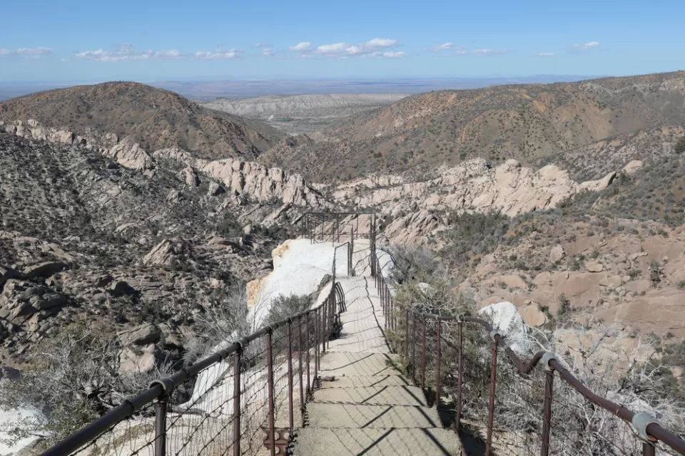 View of hiking trail descending into desert mountains with steps carved into stone and guardrails at Devil's Punchbowl Natural Area, Los Angeles County